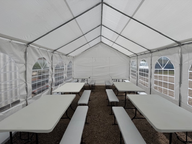 Intérieur d'une tente de réception aménagée avec tables et bancs